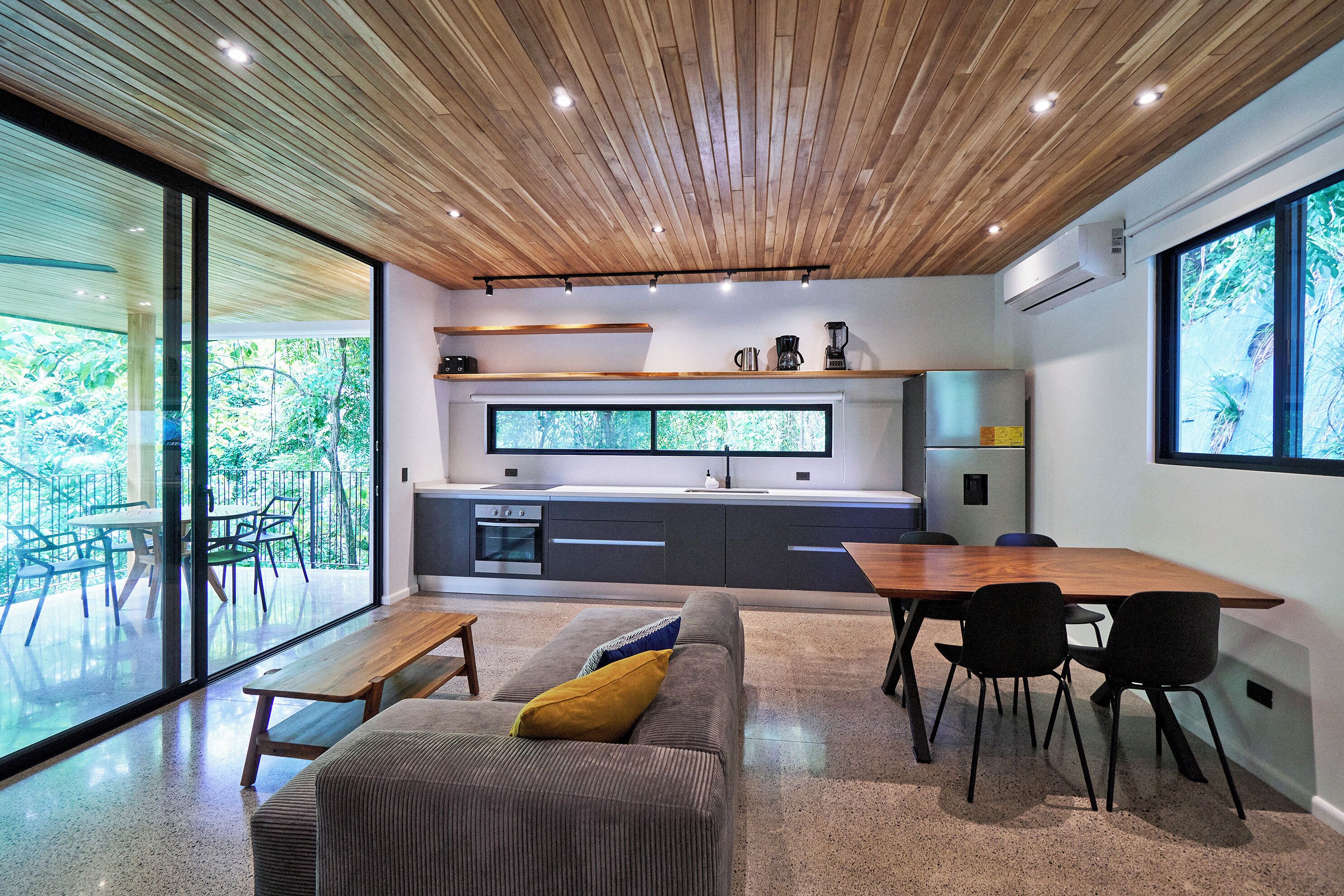 A modern kitchen with a wooden ceiling, large windows, and a dining area with a wooden table and chairs.