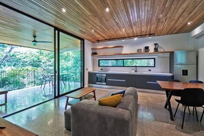 A modern kitchen with a large window, a dining area with a wooden table, and a living space with a sofa. - Casas Alba (Cóbano)
