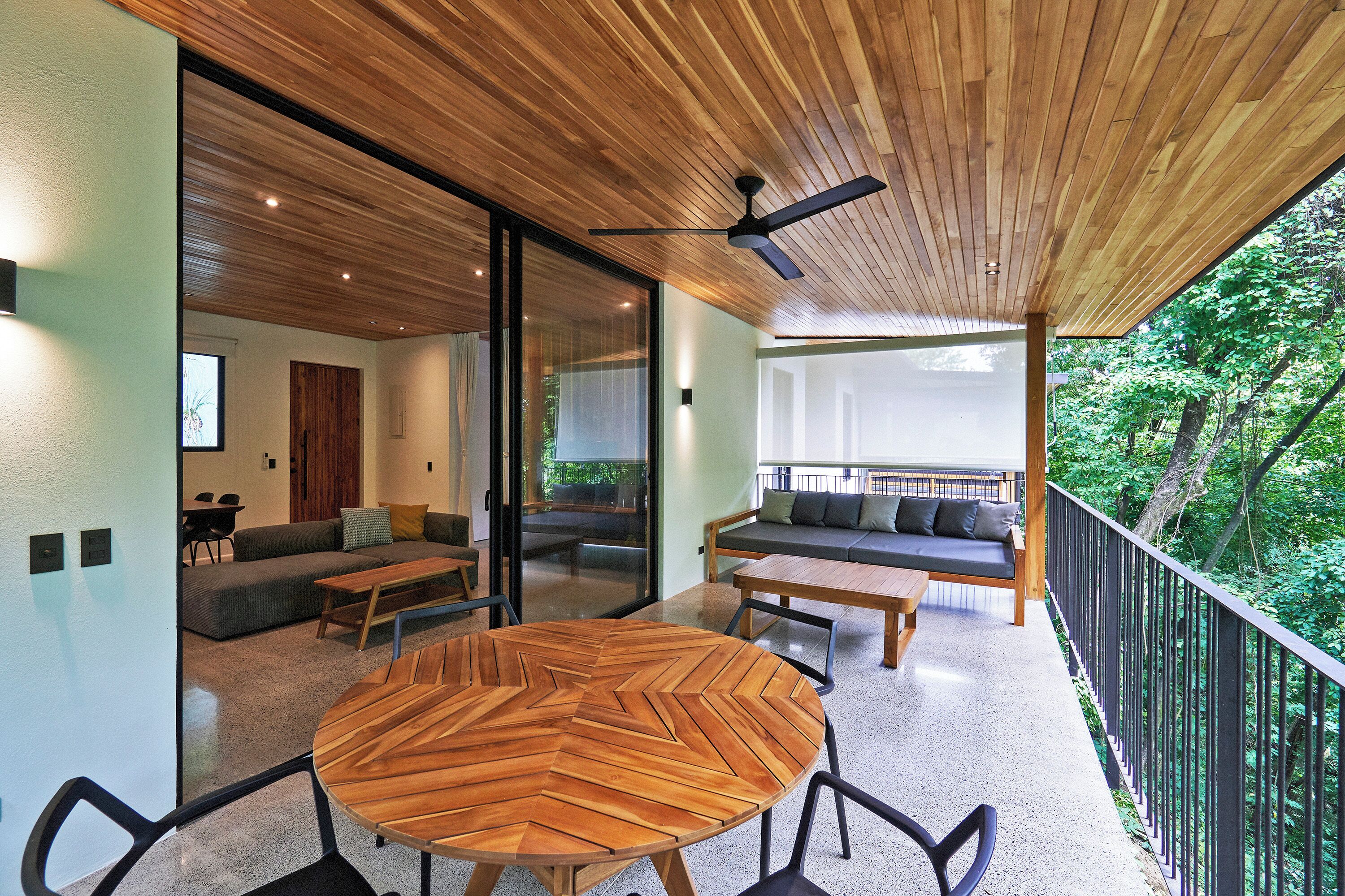 A modern interior with a wooden ceiling, a round wooden table, and a balcony with a view of greenery.