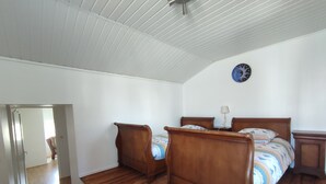 A bedroom with two wooden beds, a wooden floor, a white ceiling, and a clock on the wall. - Maison Bretonne à la Pointe du Raz (Plogoff)