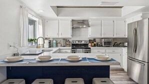 Eine moderne Küche mit weißen Schränken, einer zentralen Kochinsel mit Hockern, einem eingebauten Backofen und einem Kühlschrank.