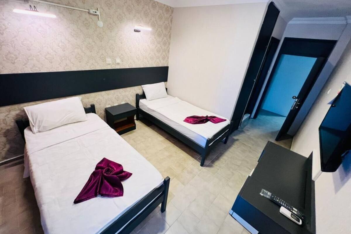 A hotel room with two beds, a desk, a TV, and a door.