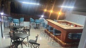 An outdoor dining area with tables and chairs, a bar area with stools, and a thatched roof structure in the background. - Blue Golden Sea (Kusadasi)