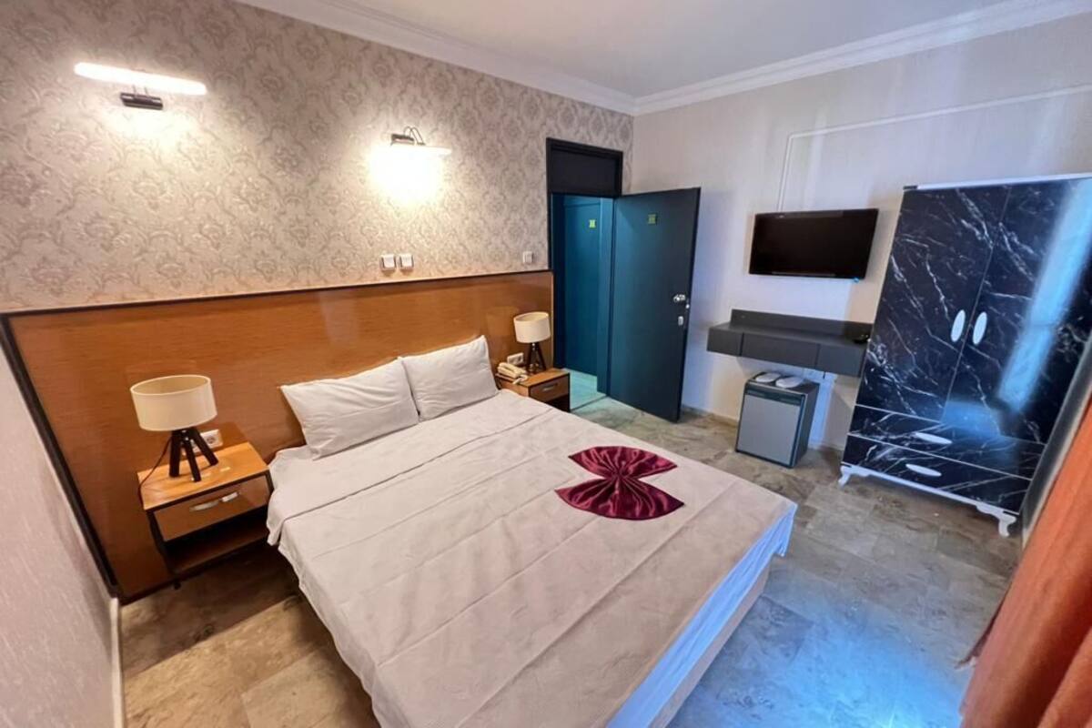 A hotel room with a bed, nightstands, a desk, a TV, and a wardrobe.