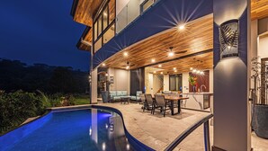 A modern house with a swimming pool, outdoor dining area, and a well-lit interior.