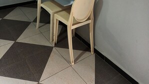 Una habitación con una mesa y dos sillas, un ventanal con vistas a un edificio y un suelo de baldosas.