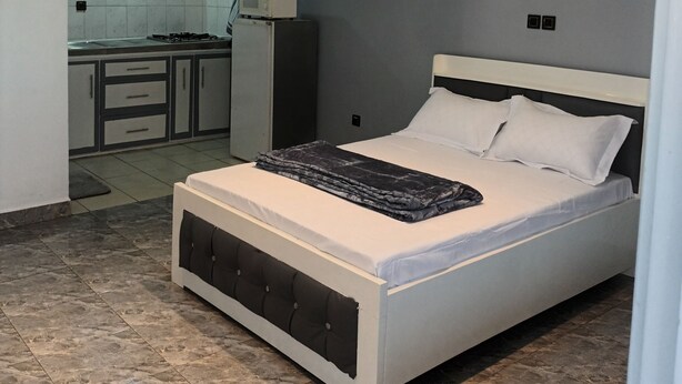 Un dormitorio moderno con una cama grande, una cocina al fondo y un techo con iluminación empotrada.