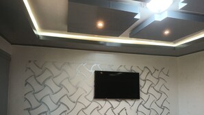 Una habitación con techo empotrado, un televisor de pantalla plana montado en una pared texturizada y un pequeño estante blanco.