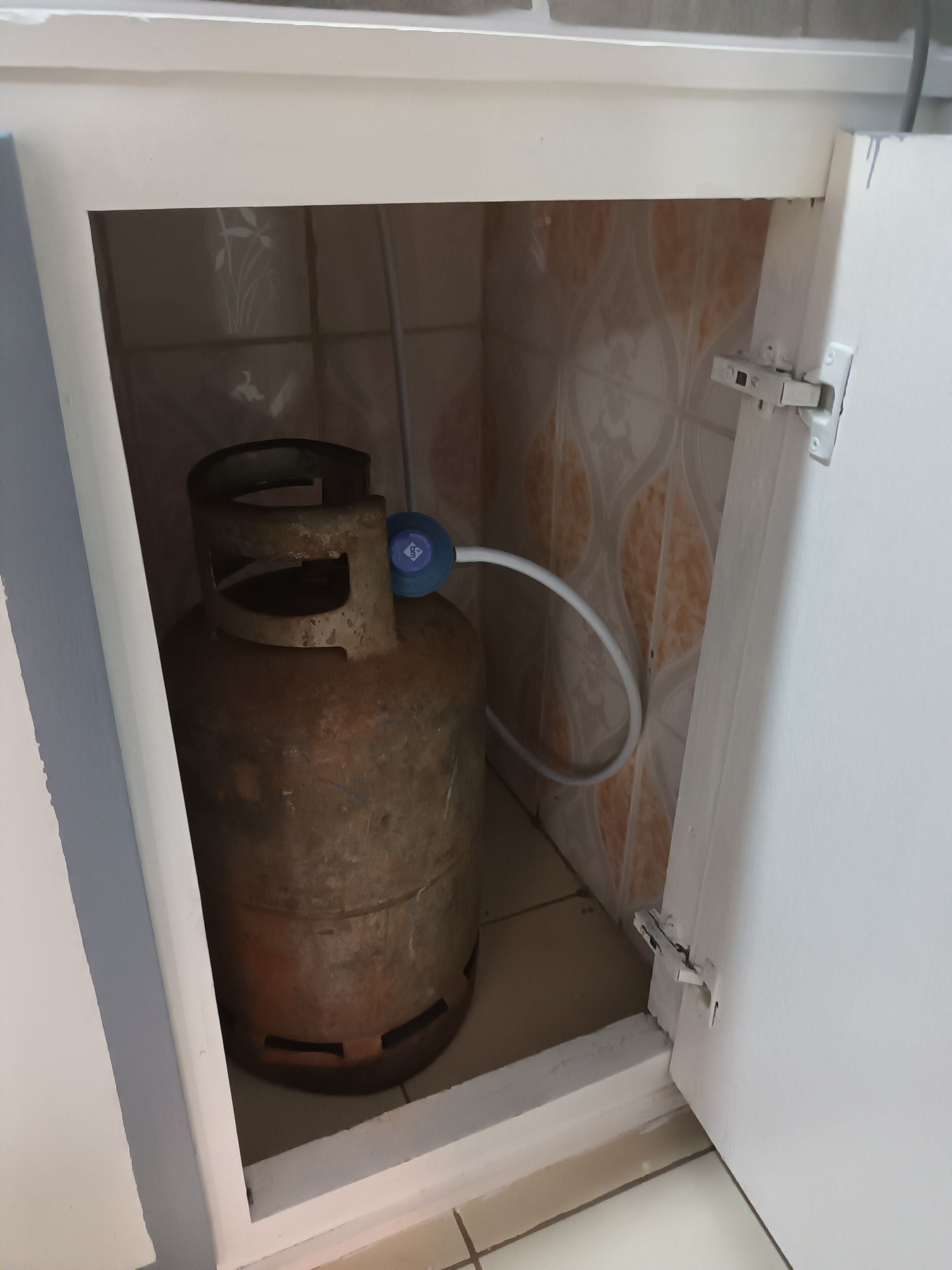 A gas cylinder under a sink with a white cabinet.