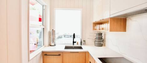 A modern kitchen with wooden cabinets, a white countertop, a black faucet, and a window with a view of a bridge.
