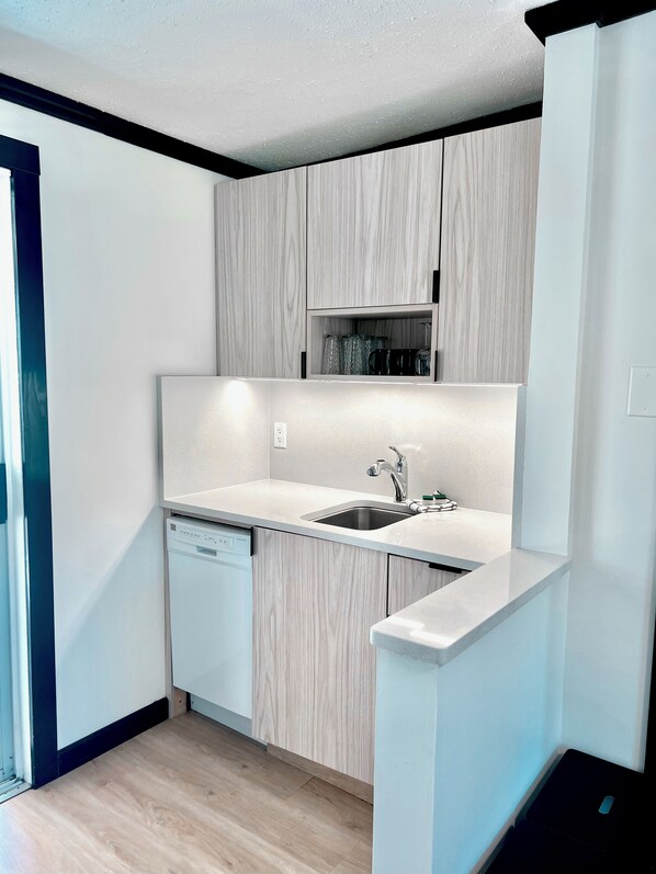 A modern kitchen with light wood cabinetry, a stainless steel sink, and a dishwasher. - Peachland Beach Resort (Peachland)