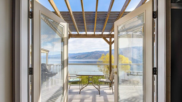 Eine offene Terrasse mit Tisch und Stühlen, einer Pergola und Blick auf einen See und Berge.