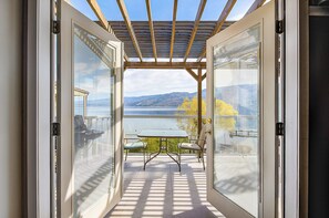 An open patio with a table and chairs, a pergola, and a view of a lake and mountains. - Peachland Beach Resort (Peachland)
