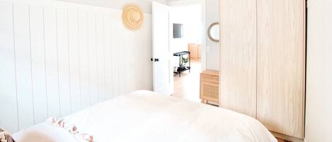 Ein Schlafzimmer mit einem Bett, einem Kleiderschrank, einer Tür zu einem anderen Raum und einem kleinen Tisch mit einer Lampe.