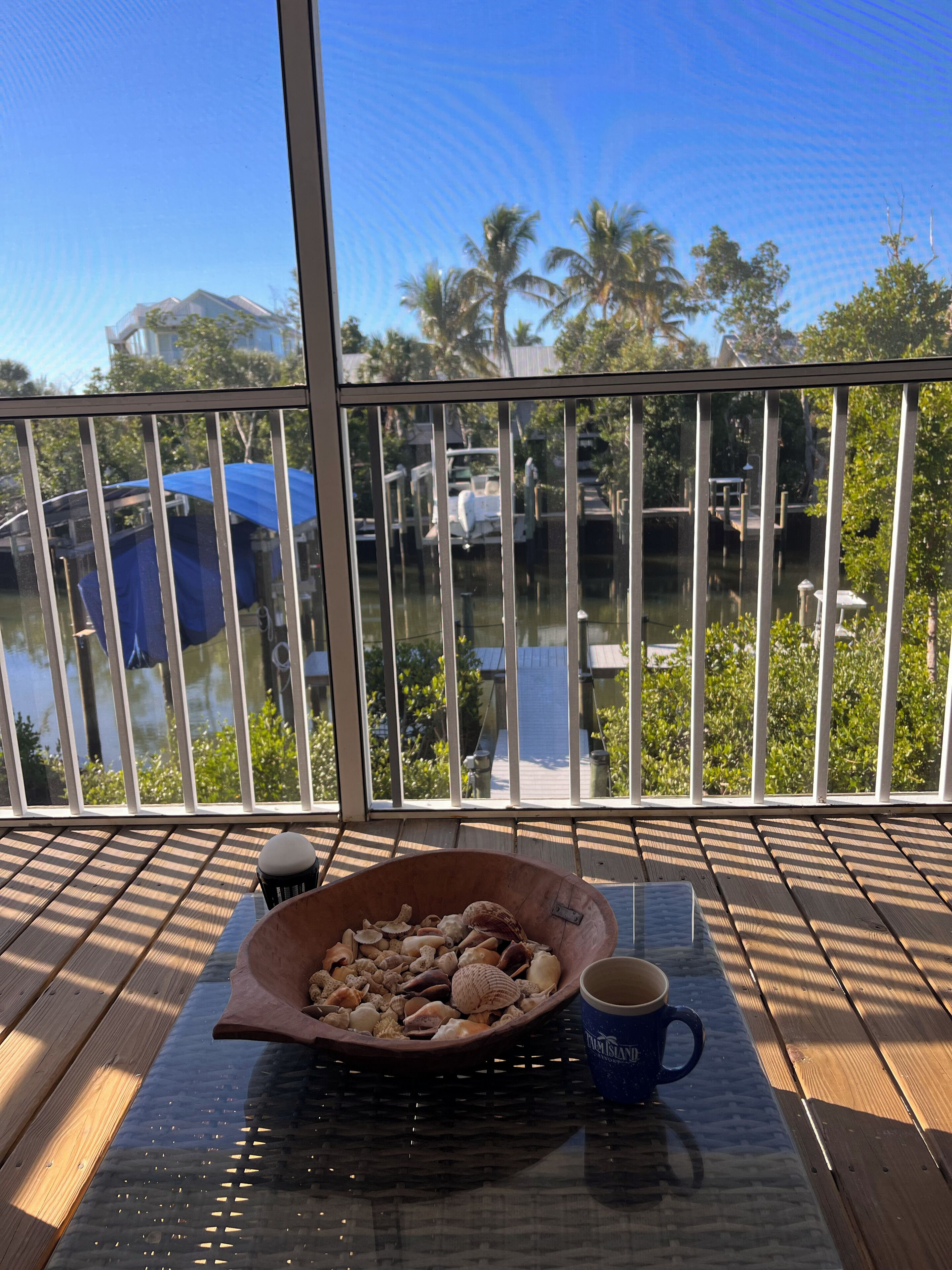 Un balcón con una mesa de madera, un cuenco de conchas marinas y una taza.