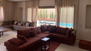 A modern living room with a sectional sofa, a coffee table, and a view of a pool and trees outside.