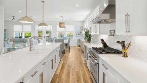 Una cocina moderna con armarios blancos, una isla central, electrodomésticos de acero inoxidable e iluminación colgante.