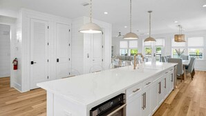 Una cocina amplia con una isla grande, armarios blancos e iluminación colgante.