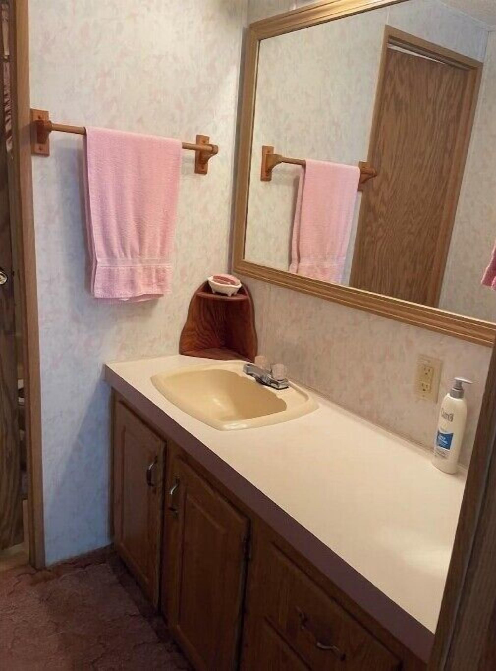A bathroom with a sink, mirror, wooden cabinets, and a pink towel hanging on a towel rack.