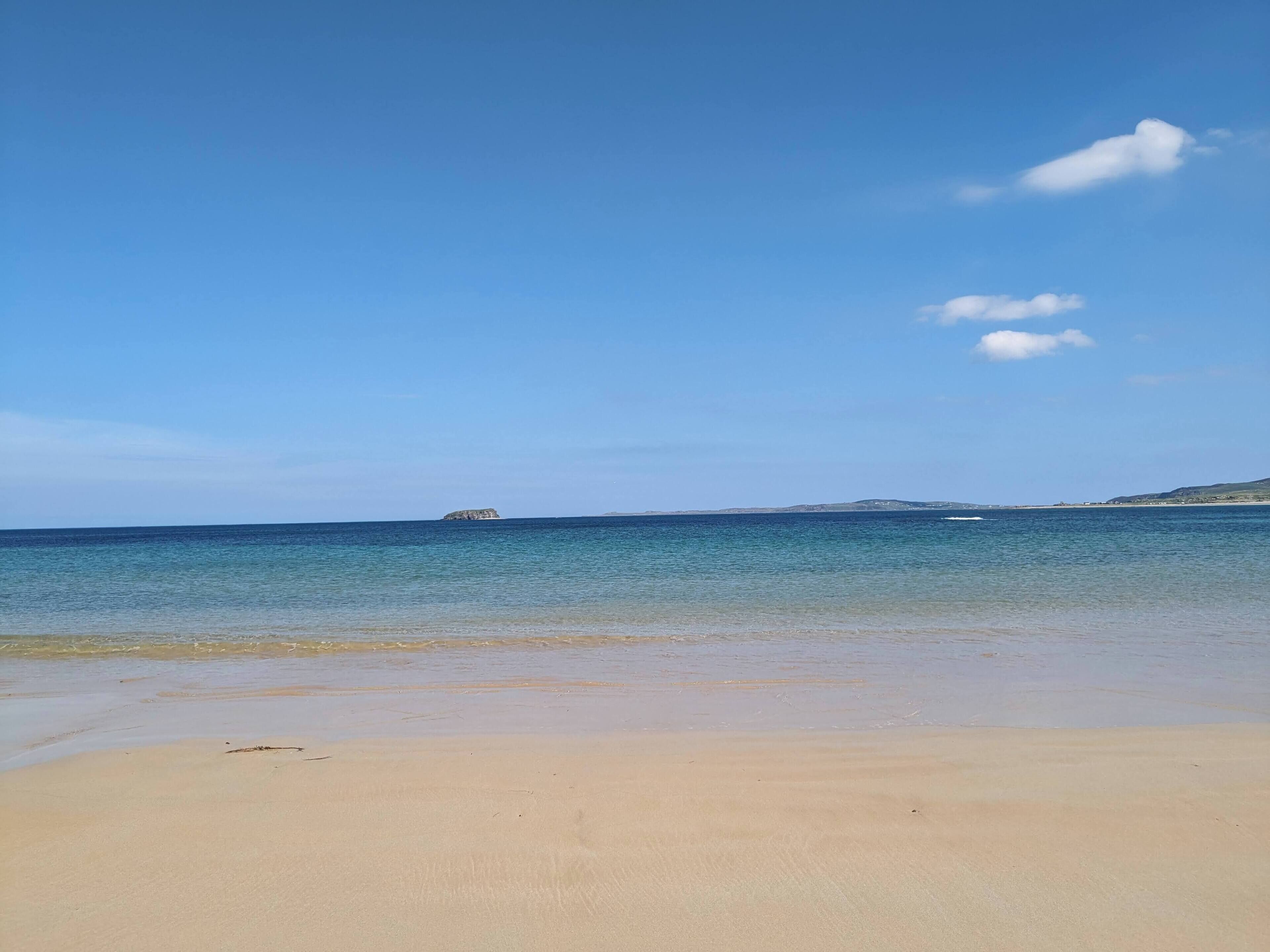 A beach with clear blue water, a sandy shore, and a distant island.