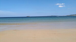 Une plage à l’eau d’un bleu cristallin, bordée d’un rivage sablonneux, avec une île qui se profile à l’horizon.