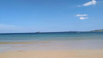 A beach with clear blue water, a sandy shore, and a distant island.
