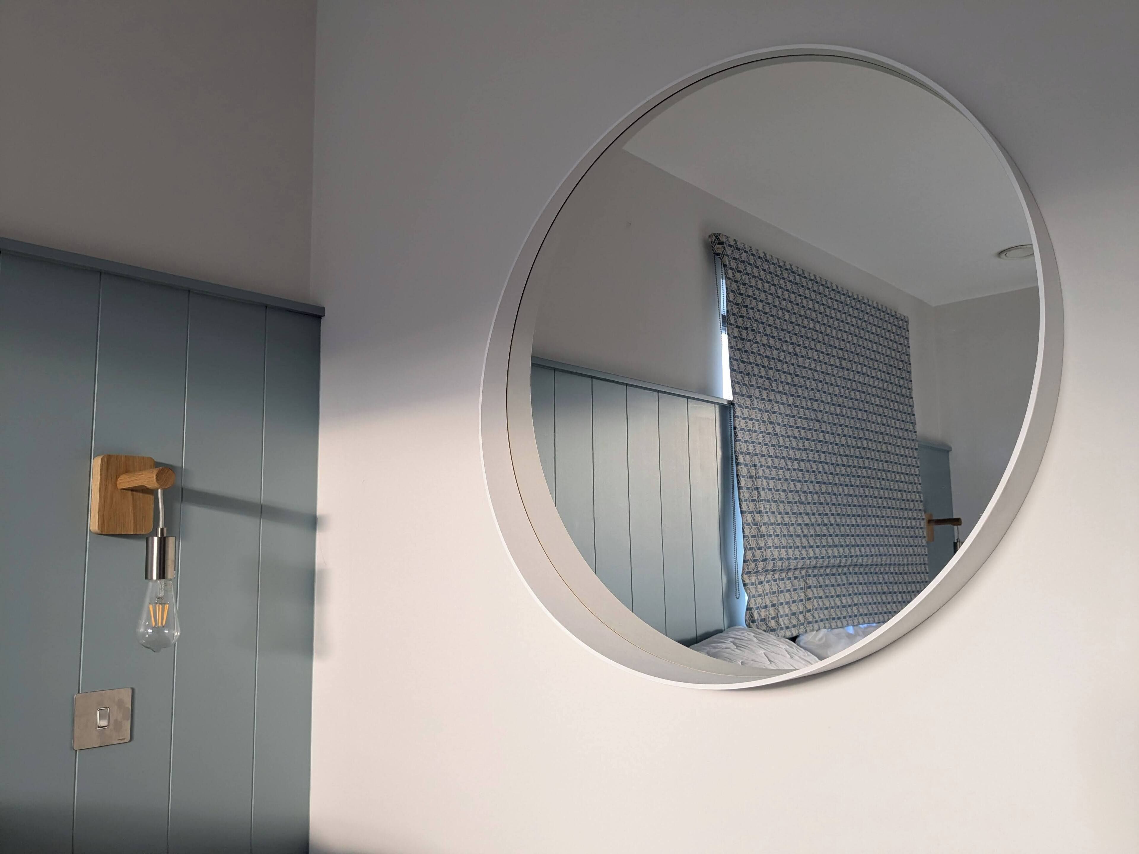 A bathroom with a round mirror, a wooden door, and a light switch.