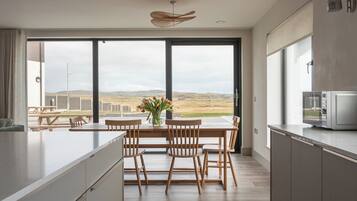 A modern kitchen with a large island, wooden chairs, and a view of the countryside through large windows.