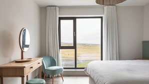Une chambre avec un grand lit, un bureau en bois avec un miroir, une chaise et une vue sur un paysage, visible à travers une porte coulissante.