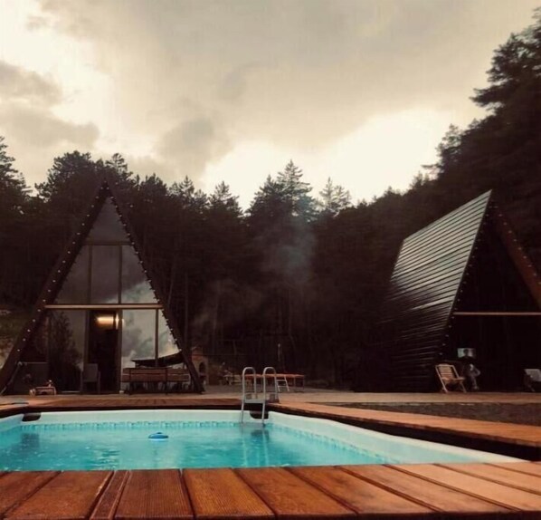Adjacent to the pool, this building offers a unique triangular design with large windows and a flat roof, blending seamlessly into the surrounding forest.