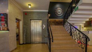 Um saguão de hotel com escadas, elevador e um relógio na parede.