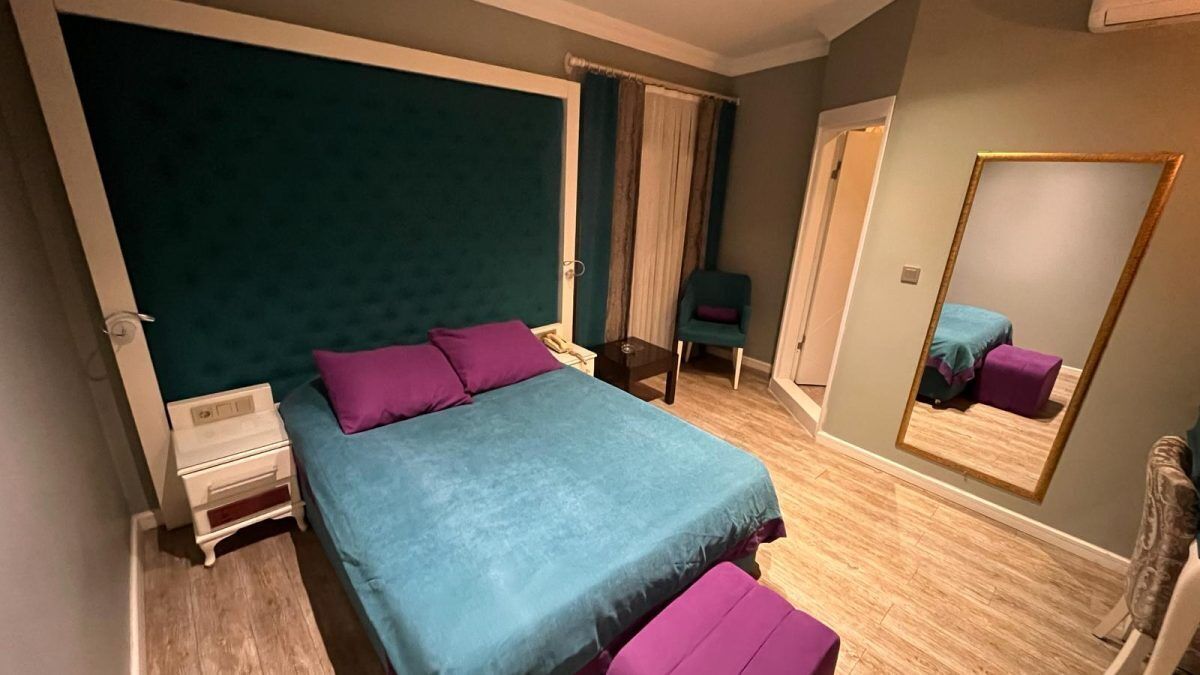A bedroom with a bed, nightstands, a chair, a mirror, and a door.