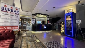 Um hall de hotel com balcão de recepção, um sofá vermelho, uma mesa de centro com tampo de vidro decorativo e um letreiro de neon azul.