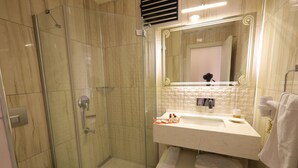 Uma casa de banho moderna com chuveiro em cabine de vidro, pia branca com artigos de higiene pessoal e um espelho grande com iluminação decorativa.