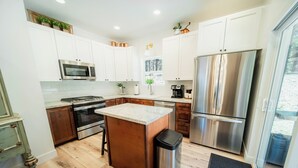 Una cocina moderna con armarios blancos, electrodomésticos de acero inoxidable, una isla de madera y vistas al exterior.
