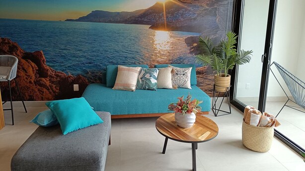 A modern living room with a large window, a sofa, a coffee table, and a view of the sea.