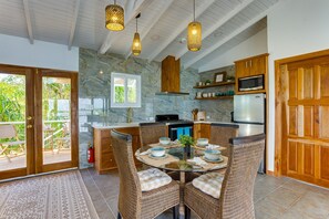 A kitchen with stone walls, wooden cabinets, and a dining area with wicker chairs and a glass table. - Luxurious Lagoon Home w/ Elegant Decor & Pool (Placencia)