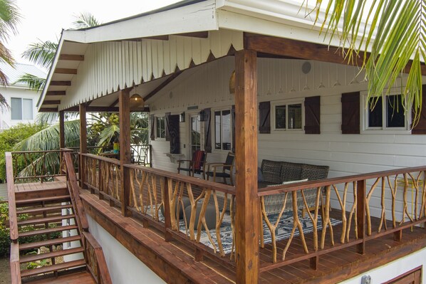 Une terrasse en bois dotée d’une rambarde, d’un escalier et d’un espace de détente abrité, avec des chaises et une table.