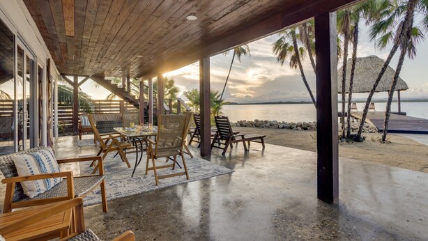 Un espace extérieur abrité, aménagé avec du mobilier en bois, offrant une vue sur la plage et l’océan.