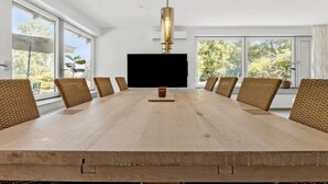 A conference room with a large table, eight wicker chairs, a flat-screen TV, and large windows with a view of trees.