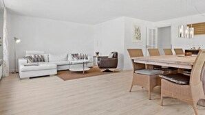 A modern living room with a white sofa, a round coffee table, and a dining area with wicker chairs and a wooden table.