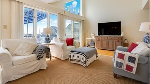 A living room with a white sofa, a grey sofa, a TV, and a window with a view of the outside. - Ocean views on Gooch's Beach! (Kennebunk)