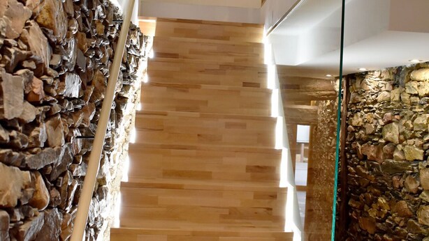 A staircase with wooden steps leading to a higher floor, flanked by stone walls and a glass railing. - Un Lujo a tu Alcance (Salamanca)