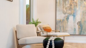 Un salon moderne avec une table basse ronde en bois, un fauteuil beige, une petite table d’appoint et un grand tableau abstrait accroché au mur.