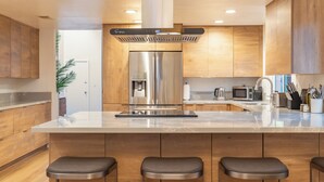 Une cuisine moderne équipée d’un réfrigérateur en acier inoxydable, d’un distributeur d’eau, d’un four à micro-ondes et d’un évier. On y trouve des armoires en bois et un plan de travail en marbre.