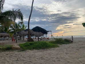 A beach with thatched umbrellas, palm trees, and a sunset view. - Las acacias Tolu (Tolú)
