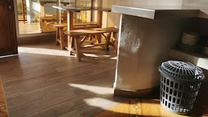 A room with a wooden floor, a large window with a view of palm trees, a wooden table, and a laundry basket. - Las acacias Tolu (Tolú)