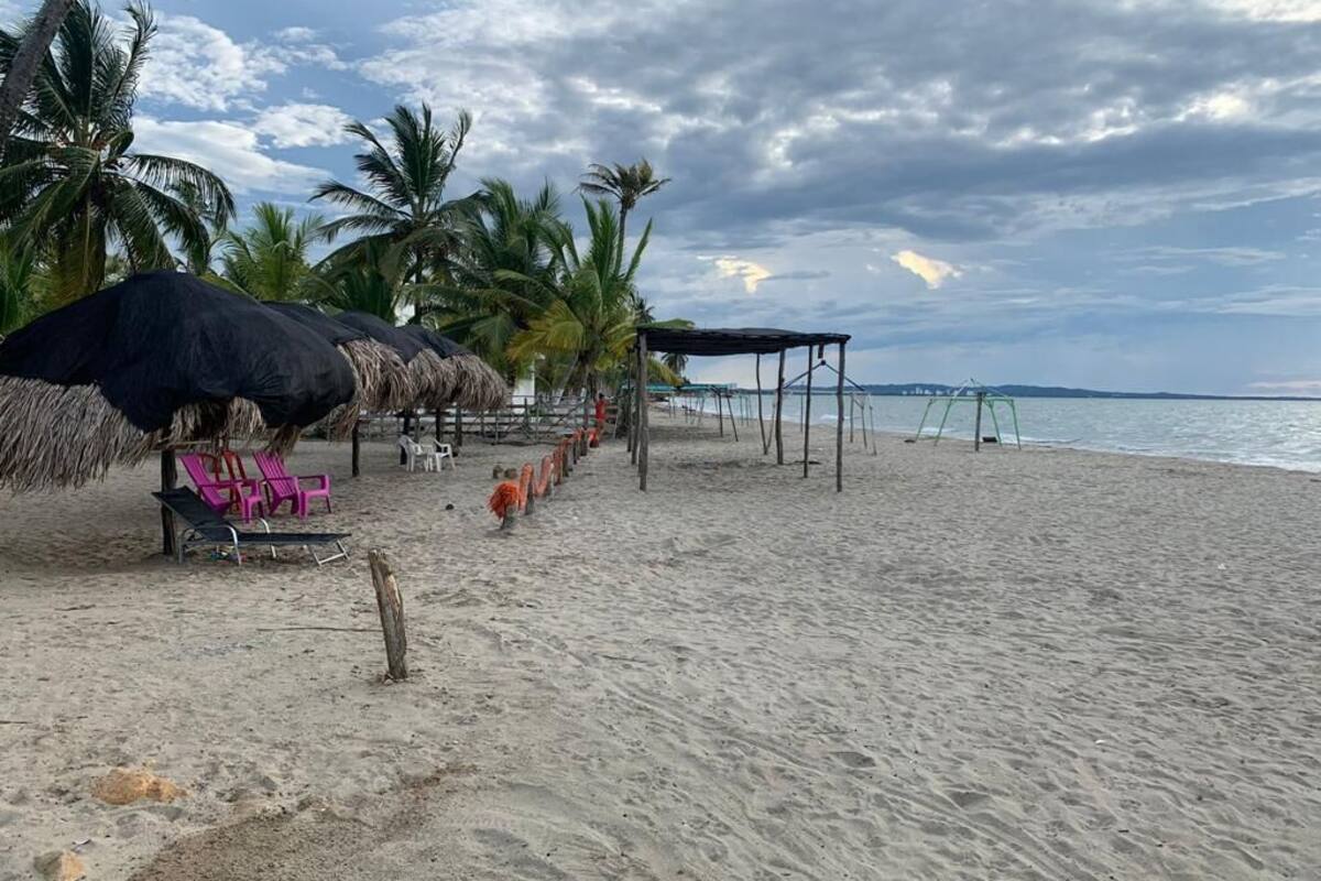 Una playa con sombrillas de paja, sillas de descanso y una estructura de madera.