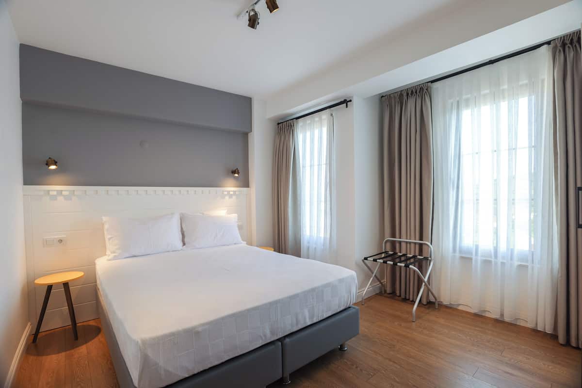 A modern bedroom with a large bed, a bedside table, a hanging chair, and a window with curtains.