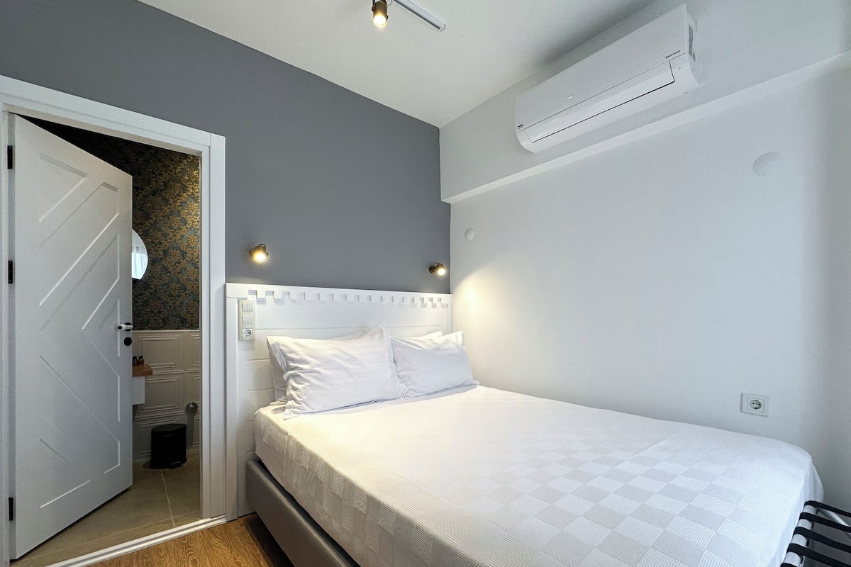 A bedroom with a bed, a door, an air conditioning unit, and a wall-mounted light fixture.